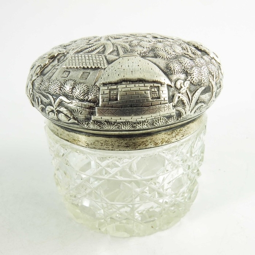 19 - A 19th century Oriental white metal lidded cut glass jar, repousse decorated and etched with village... 