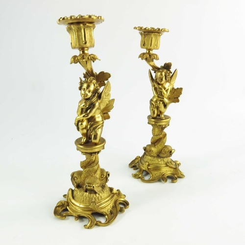 554 - A Pair of 19th Century Gilt Bronze Candlesticks, each modelled with winged cherubs mounted on circul... 