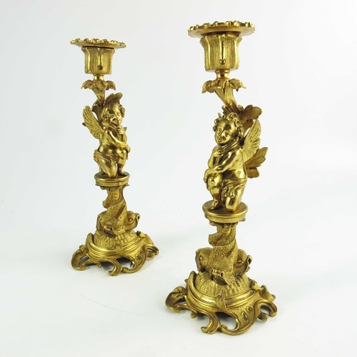 554 - A Pair of 19th Century Gilt Bronze Candlesticks, each modelled with winged cherubs mounted on circul... 