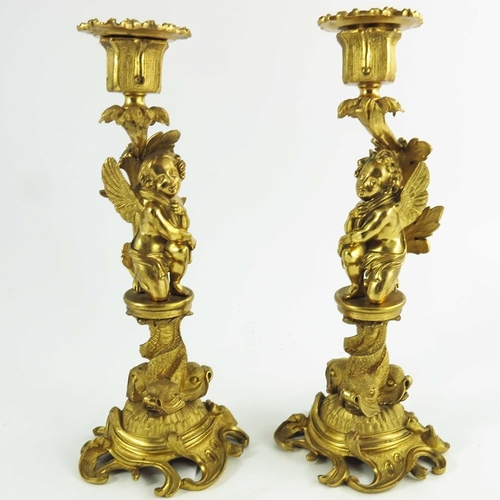 554 - A Pair of 19th Century Gilt Bronze Candlesticks, each modelled with winged cherubs mounted on circul... 