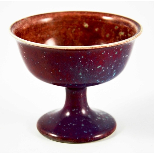 1341 - A Ruskin high fired Melba cup, circa 1920, pedestal ogee form, red with speckled purple and green, i... 