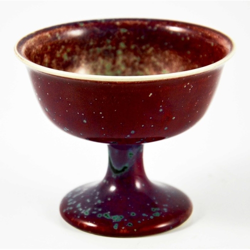 1341 - A Ruskin high fired Melba cup, circa 1920, pedestal ogee form, red with speckled purple and green, i... 