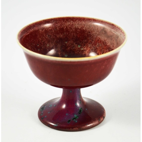 1350 - A Ruskin high fired Melba cup, circa 1920, pedestal ogee form, red with speckled purple and green, i... 