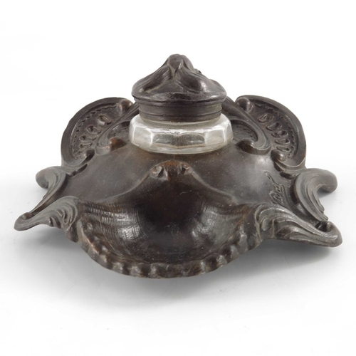 493 - N Vidal, an Art Nouveau bronzed inkwell, cast in relief with foliate scrolls and shells, faceted gla... 