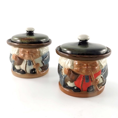 664 - Harry Simeon for Doulton Lambeth, two stoneware Toby jars, modelled smoking pipes, one with red wais... 