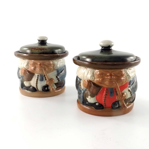 664 - Harry Simeon for Doulton Lambeth, two stoneware Toby jars, modelled smoking pipes, one with red wais... 