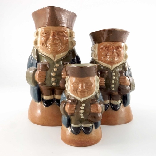 668 - Harry Simeon for Doulton Lambeth, a graduated set of three Toby jugs, each modelled with bottle and ... 