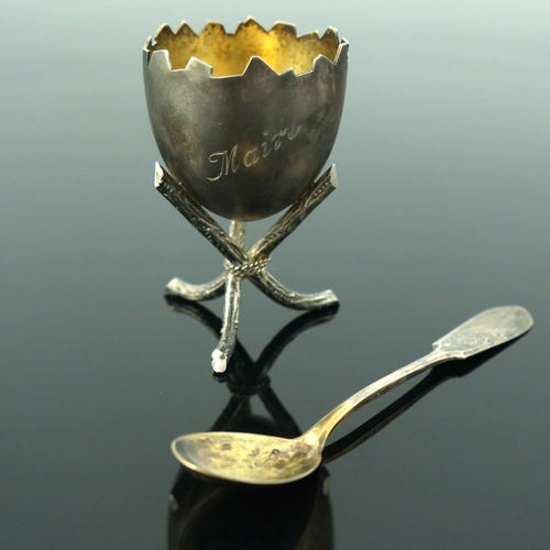 52 - A Finnish novelty silver egg cup and spoon, Suomen Kultaseppa Oy, Turku 1911, modelled as broken hal... 