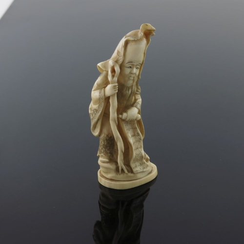 510 - λ A Japanese ivory okimono, Meiji period, 1868-1912, carved as a robed bearded immortal standing hol... 