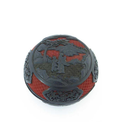 411 - A Chinese red and black lacquer circular covered vessel, carved in high relief with two figures in a... 