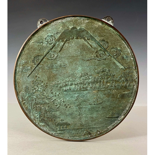 418 - A Japanese bronze roundel wall plaque, cast with a landscape scene with pagodas and boats on a lake ... 