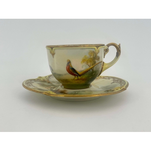 928 - Hadley's Worcester, a cabinet cup and saucer, lobed and painted with a pheasant in open countryside,... 