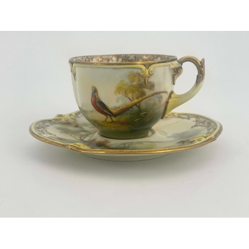 928 - Hadley's Worcester, a cabinet cup and saucer, lobed and painted with a pheasant in open countryside,... 