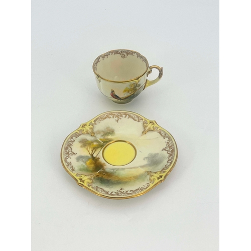 928 - Hadley's Worcester, a cabinet cup and saucer, lobed and painted with a pheasant in open countryside,... 