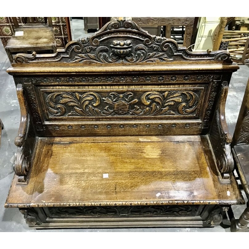 824 - A carved oak box settle, with urn carved pediment, carved scroll arms, lift up seat and carved front... 