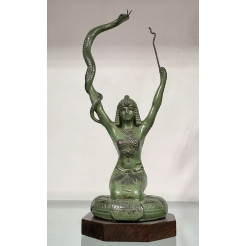 438 - An Art Deco patinated art metal figure modelled as an Egyptian snake tamer, arms raised, on wooden b... 