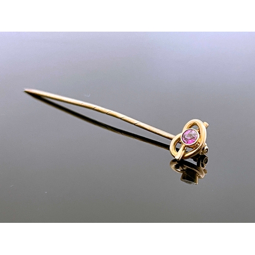 181 - A 9 carat gold and pink gem set stick pin, the knotted wire head set with a facet cut stone, 5.5cm l... 