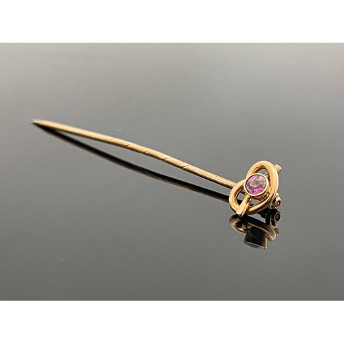 181 - A 9 carat gold and pink gem set stick pin, the knotted wire head set with a facet cut stone, 5.5cm l... 