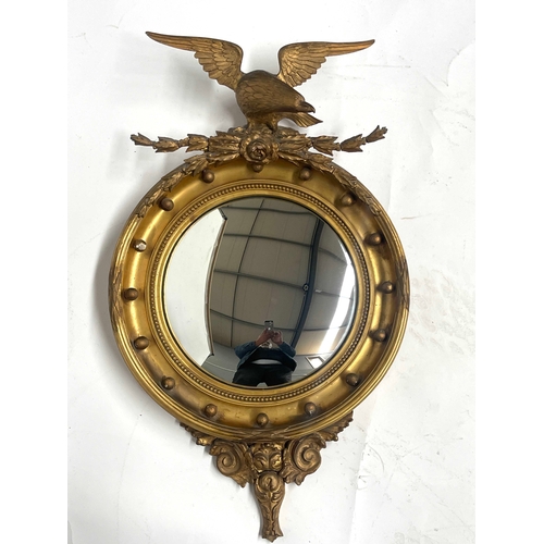 230 - A carved gilt wood convex looking glass, 19th Century, American Federal style eagle pediment, ball b... 