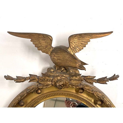 230 - A carved gilt wood convex looking glass, 19th Century, American Federal style eagle pediment, ball b... 