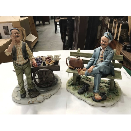 327 - Two Capodimonte figures, fruit seller and cart, 28cm high, and seated postman, 23cm high (2)