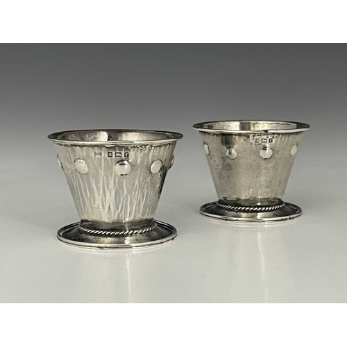 94 - Bernard Cuzner, a pair of Arts and Crafts silver salt cellars, Birmingham 1905, conical footed bucke... 