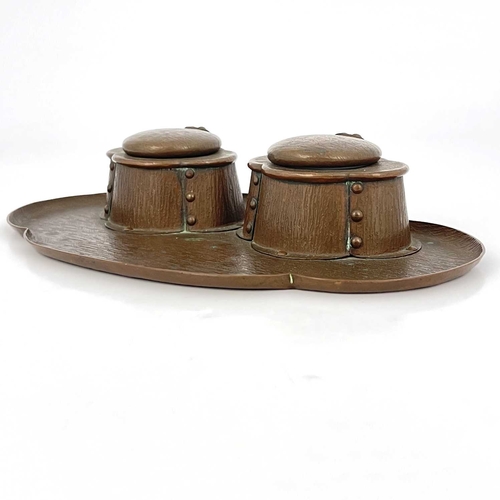 154 - An Arts and Crafts copper double inkwell, bark textured, the quatrefoil oval tray with two rivetted ... 