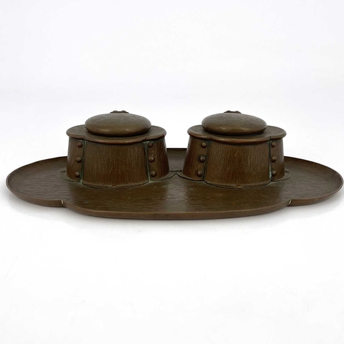 154 - An Arts and Crafts copper double inkwell, bark textured, the quatrefoil oval tray with two rivetted ... 