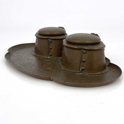 154 - An Arts and Crafts copper double inkwell, bark textured, the quatrefoil oval tray with two rivetted ... 