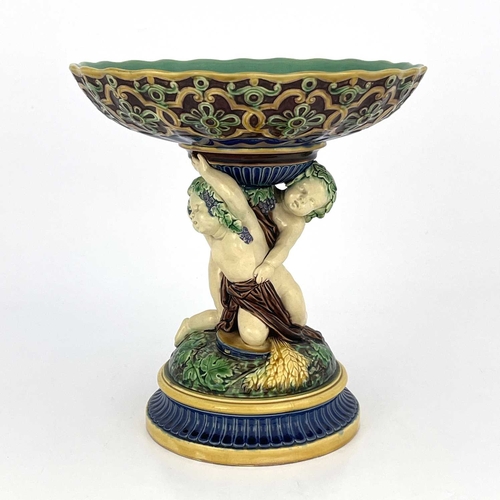 792 - A Minton majolica figural comport, 1863, modelled as two Bacchanalian putti on a vine moulded domed ... 