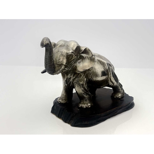 313 - A white metal model of a strolling elephant with trunk raised, mounted on a wooden plinth, 13cm high... 