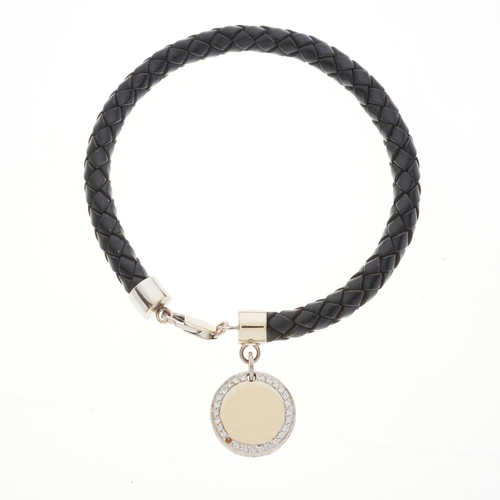 176 - An 18ct gold diamond accent disc charm, suspended from a woven leather bracelet, estimated total dia... 