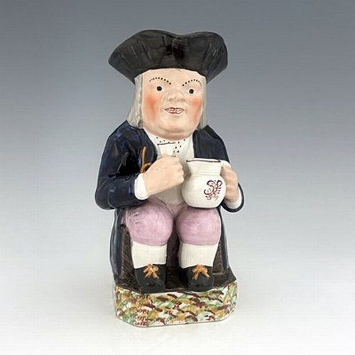 1003 - A Mexborough Toby jug, modelled holding a jug and a beaker, caryatid figural handle, black hat and s... 