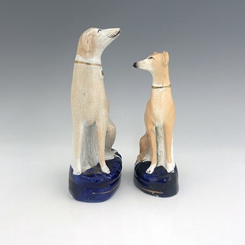 1024 - Two Staffordshire pearlware greyhounds, circa 1840, painted in light brown enamel, seated on cobalt ... 