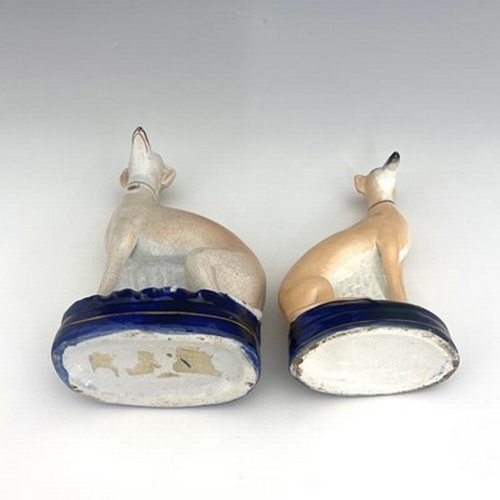 1024 - Two Staffordshire pearlware greyhounds, circa 1840, painted in light brown enamel, seated on cobalt ... 