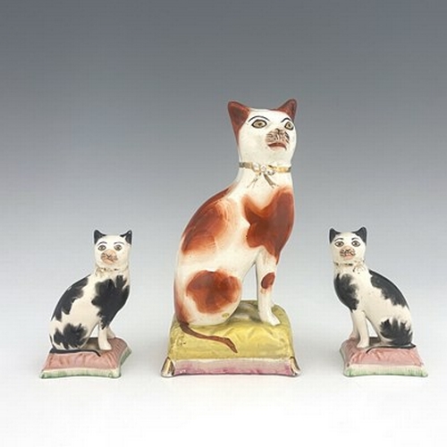 1036 - Three Staffordshire pottery cats, 19th century, including a pair of black and white cats on pink cus... 