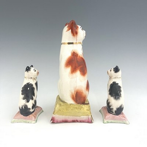 1036 - Three Staffordshire pottery cats, 19th century, including a pair of black and white cats on pink cus... 