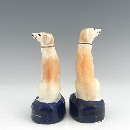 1043 - A pair of Staffordshire greyhounds, circa 1860, painted in light brown enamel, seated on cobalt blue... 