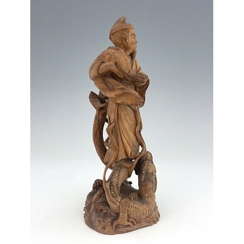 588 - A Chinese carved figure of a scholar, modelled holding a scroll, standing on a writhing dragon, 21cm... 