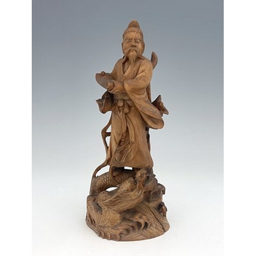 588 - A Chinese carved figure of a scholar, modelled holding a scroll, standing on a writhing dragon, 21cm... 