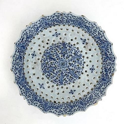 786 - A Dutch Delft blue and white strainer dish, on three legs, ogee rim, foliate scroll panel border aro... 