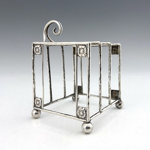 93 - A E Jones, an Arts and Crafts silver three division toast rack, Birmingham 1918, planished wire cons... 