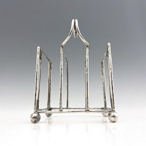 93 - A E Jones, an Arts and Crafts silver three division toast rack, Birmingham 1918, planished wire cons... 