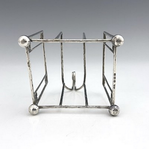 93 - A E Jones, an Arts and Crafts silver three division toast rack, Birmingham 1918, planished wire cons... 