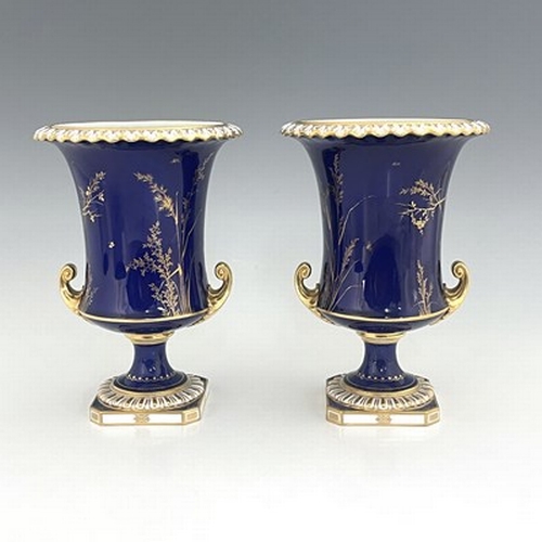 941 - Albert Gregory for Roal Crown Derby, a pair of twin handled Campana Urn vases, 1920, painted with fl... 