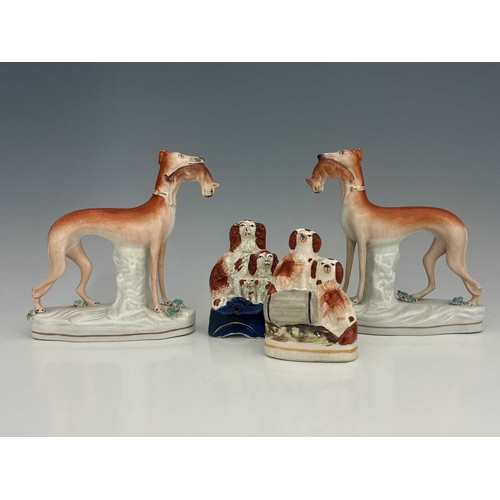 735 - A pair of Staffordshire pottery figures of greyhounds, modelled standing, holding rabbits, on tufted... 