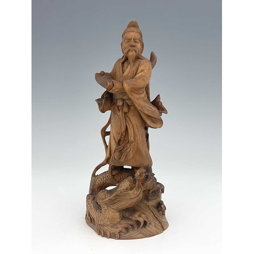 411 - A Chinese carved figure of a scholar, modelled holding a scroll, standing on a writhing dragon, 21cm... 