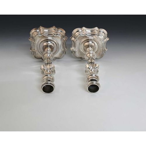 63 - A pair of George II silver cast candlesticks, each on a shaped stepped square base, with baluster st... 