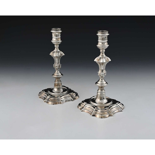 63 - A pair of George II silver cast candlesticks, each on a shaped stepped square base, with baluster st... 