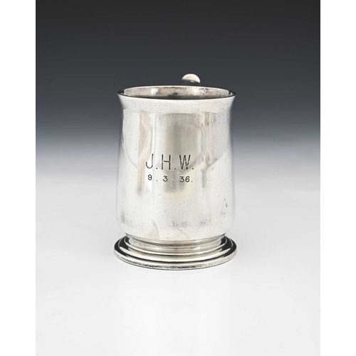 67 - A George V silver mug, with C-scroll handle, and raised thumbpiece, atop a stepped circular form foo... 